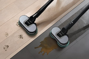 Two wet floor buffers with black handles and gray pads are shown cleaning a light wood floor and a dark glossy floor, with a puddle of water on the dark surface.